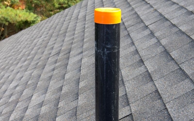 A black plumbing vent pipe protrudes above a shingled roof.