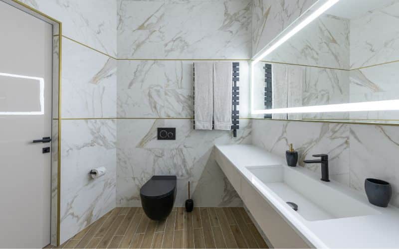A modern bathroom featuring marble walls and a white sink, with the water supply line running through the floor for toilet functionality.