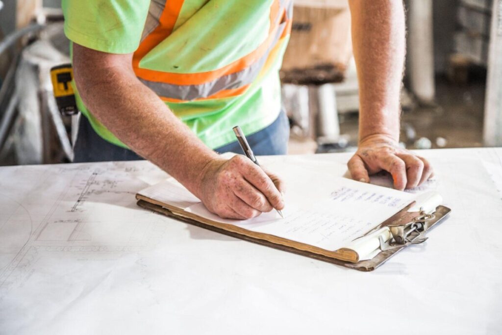 A construction worker is writing on a clipboard.