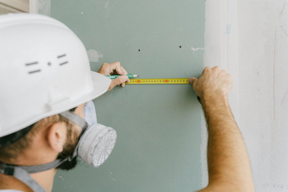 A man in a hard hat is measuring the wall with a tape measure.